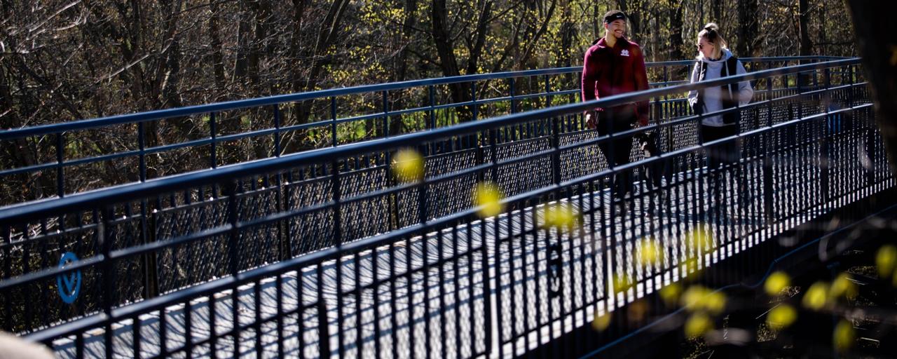Two individuals walking along the Little Mac Bridge in the springtime